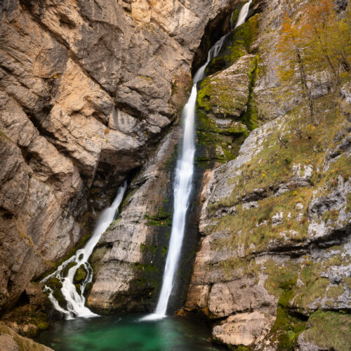 Cascada de agua turquesa cayendo entre acantilados rocosos cubiertos de musgo verde en un cañón estrecho
