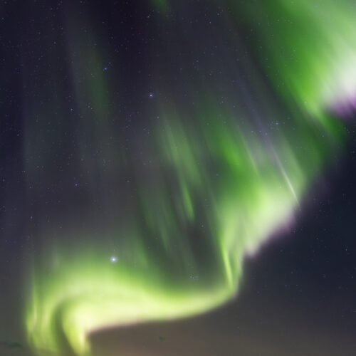 Aurora boreal verde y púrpura danzando sobre montaña nevada en Abisko, bajo cielo estrellado nocturno