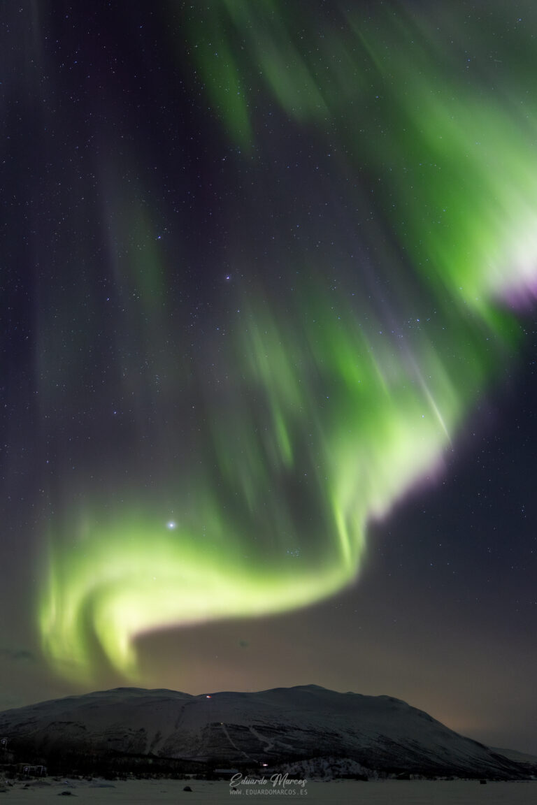 Aurora boreal verde y púrpura danzando sobre montaña nevada en Abisko, bajo cielo estrellado nocturno