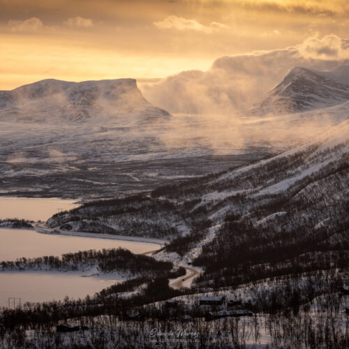 Montañas nevadas con lagos helados y bosque de abedules bajo cielo dorado al atardecer en Abisko