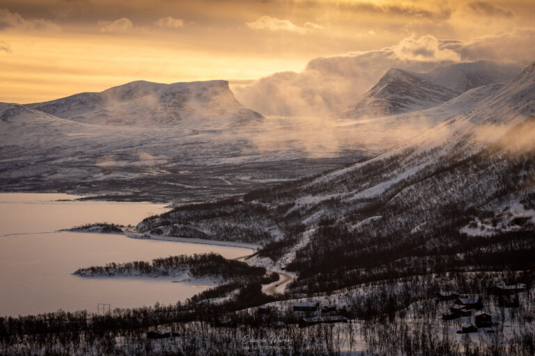 Montañas nevadas con lagos helados y bosque de abedules bajo cielo dorado al atardecer en Abisko