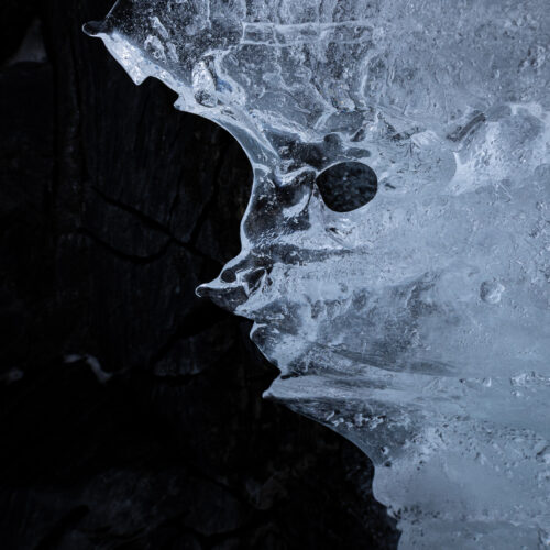 Formación de hielo con estructura de cráneo en la orilla de un lago congelado, contraste entre hielo translúcido y agua oscura