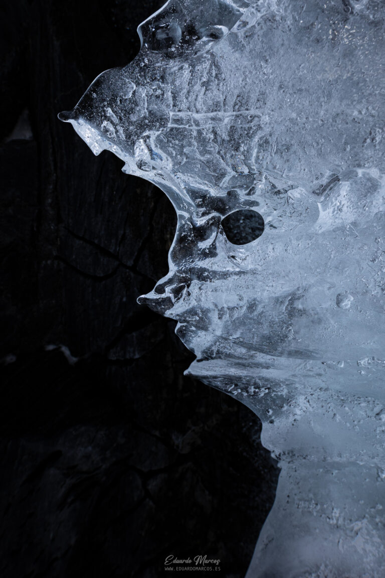 Formación de hielo con estructura de cráneo en la orilla de un lago congelado, contraste entre hielo translúcido y agua oscura