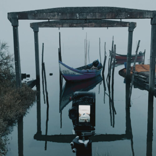 Cámara de película sobre trípode enfocando góndolas tradicionales amarradas en la brumosa ría de Aveiro