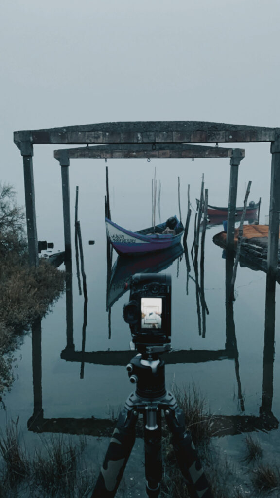 Cámara de película sobre trípode enfocando góndolas tradicionales amarradas en la brumosa ría de Aveiro
