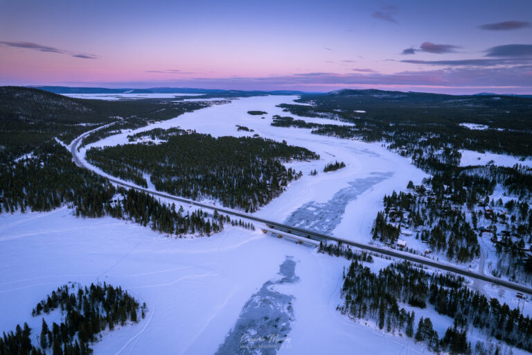 Río congelado rodeado de bosque boreal al atardecer, con carretera atravesando el paisaje nevado de Abisko