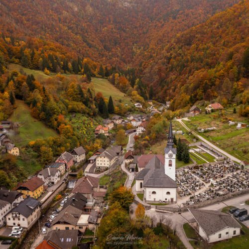 Valle alpino con pueblo, iglesia blanca y bosque otoñal en montañas densamente arboladas