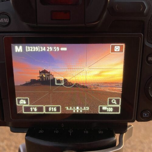 Pantalla de cámara profesional mostrando una capilla al atardecer sobre la playa, con configuración manual de exposición F16 y ISO 100