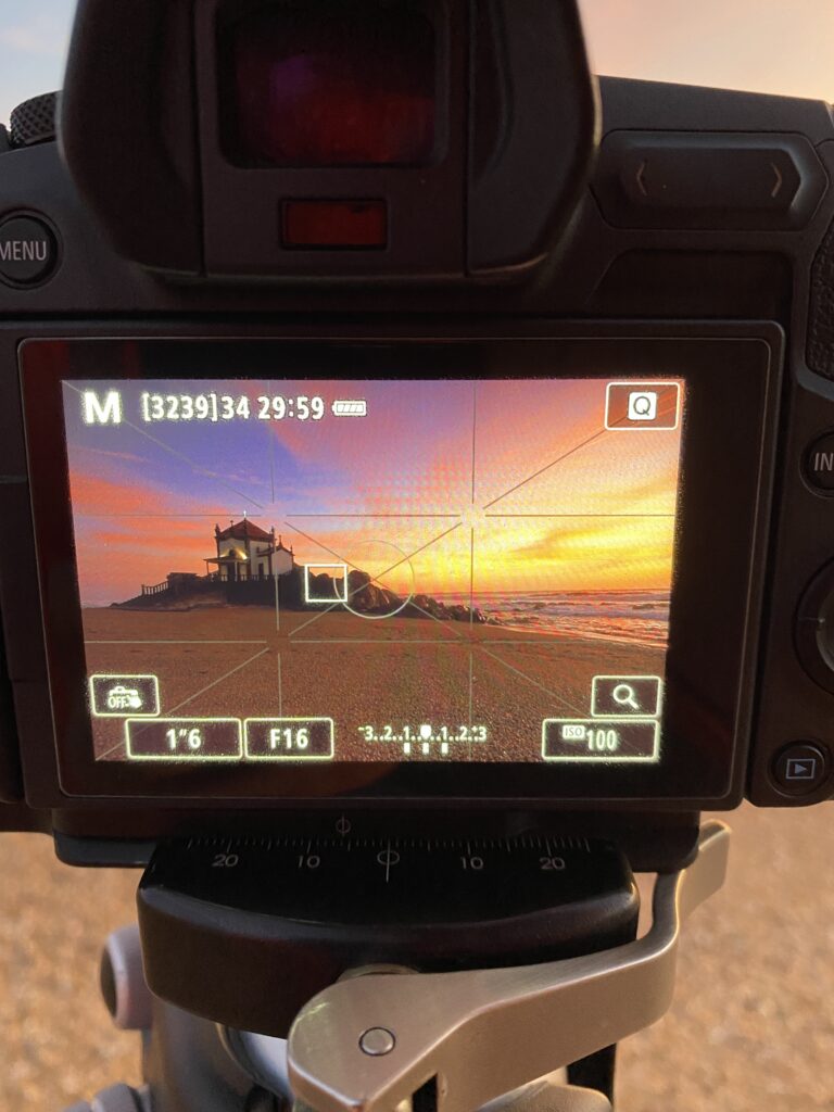 Pantalla de cámara profesional mostrando una capilla al atardecer sobre la playa, con configuración manual de exposición F16 y ISO 100