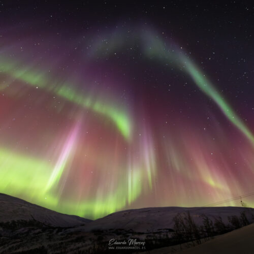 Aurora boreal verde y rosa iluminando montañas nevadas bajo cielo estrellado nocturno