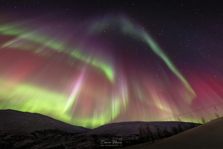 Aurora boreal verde y rosa iluminando montañas nevadas bajo cielo estrellado nocturno