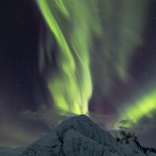 Aurora boreal verde intenso sobre montaña nevada cubierta de hielo en Abisko, Suecia, con estrellas visibles de fondo