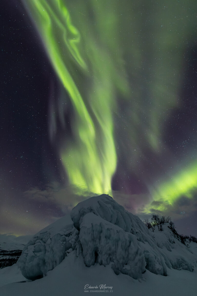 Aurora boreal verde intenso sobre montaña nevada cubierta de hielo en Abisko, Suecia, con estrellas visibles de fondo