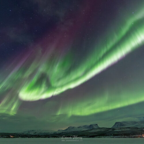 Aurora boreal verde intenso ondulante sobre montañas nevadas y lago congelado en la noche estrellada de Abisko
