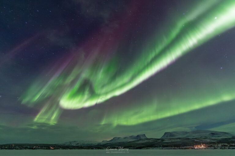 Aurora boreal verde intenso ondulante sobre montañas nevadas y lago congelado en la noche estrellada de Abisko