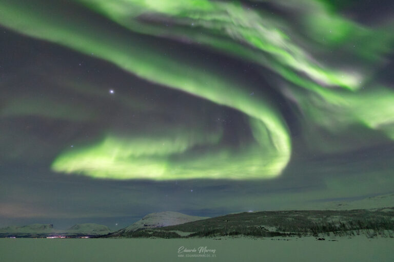 Aurora boreal verde intenso ondulante sobre paisaje nevado de Abisko con montaña al fondo y cielo estrellado